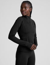 woman wearing a black long-sleeve athletic jacket with a zipper on a plain background.
